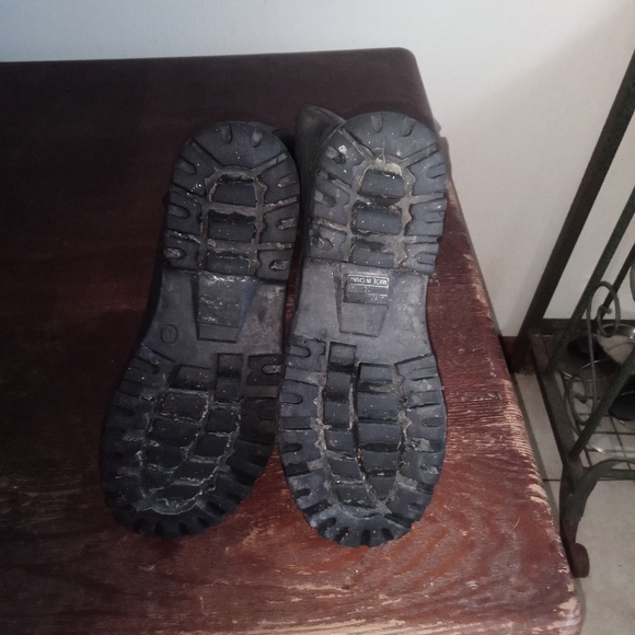 A close-up photo of a pair of black rubber boots with a worn tread sitting on a - Picture 3 of 3